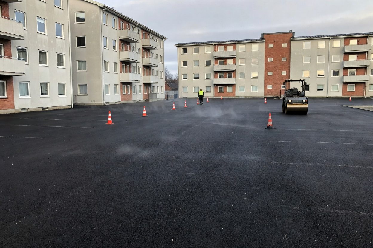 Nyasfaltert parkeringsplass ved et borettslag, med valse og kjegler